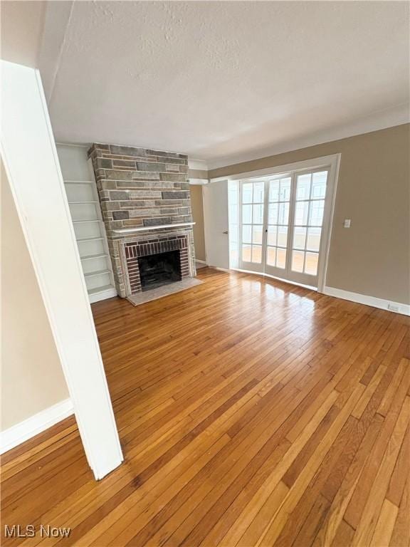 unfurnished living room featuring a large fireplace, wood-type flooring, a textured ceiling, and built in features