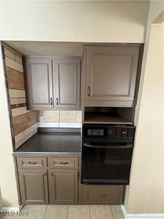 kitchen with tasteful backsplash, black oven, gray cabinets, and light tile patterned flooring