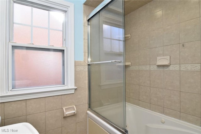 bathroom with combined bath / shower with glass door, tile walls, and toilet