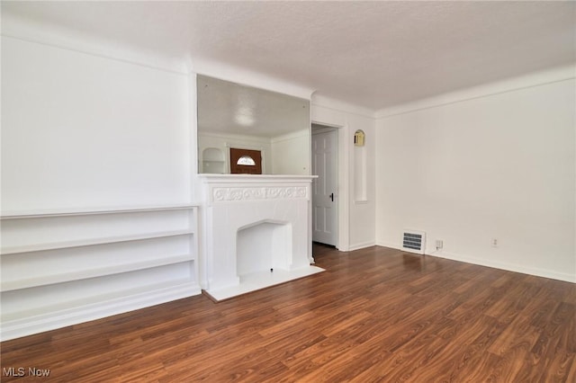 unfurnished living room with dark wood-type flooring, built in features, and a textured ceiling