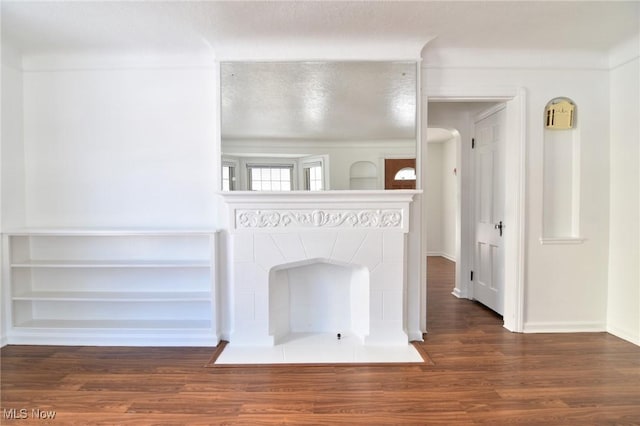 unfurnished living room featuring dark wood-type flooring, a tiled fireplace, and a textured ceiling