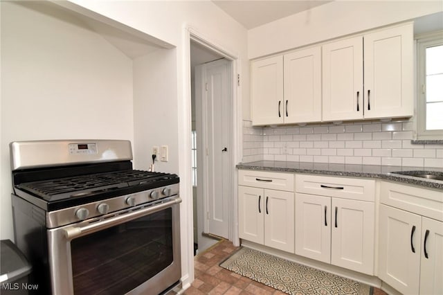 kitchen featuring stainless steel gas range oven, dark stone countertops, white cabinets, and decorative backsplash