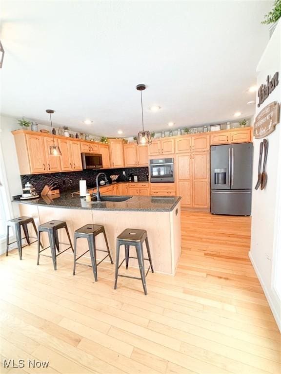 kitchen with appliances with stainless steel finishes, decorative light fixtures, sink, a breakfast bar area, and light brown cabinets