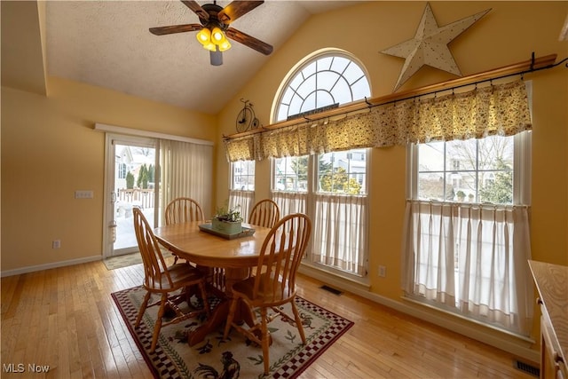 dining area featuring ceiling fan, high vaulted ceiling, a textured ceiling, and light wood-type flooring