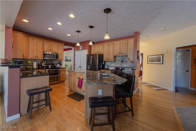 kitchen featuring a breakfast bar area, dark stone countertops, hanging light fixtures, stainless steel appliances, and a kitchen island