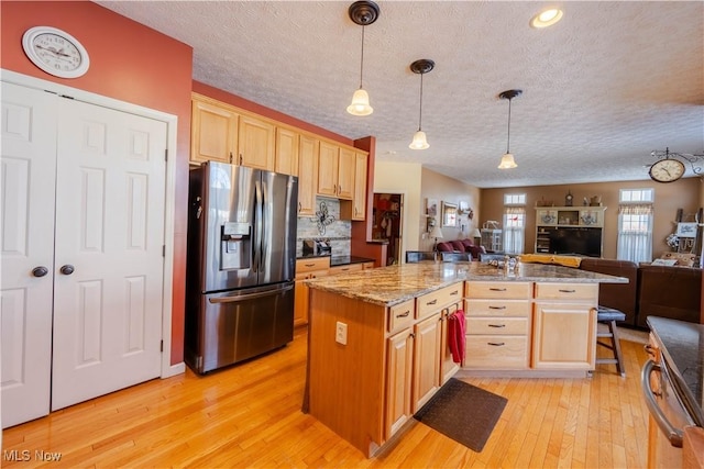 kitchen with light brown cabinetry, stainless steel fridge with ice dispenser, a breakfast bar area, and hanging light fixtures