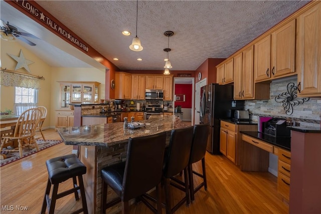 kitchen with a breakfast bar, a center island, dark stone countertops, appliances with stainless steel finishes, and pendant lighting