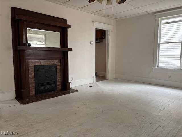 unfurnished living room with ceiling fan, a drop ceiling, a fireplace, and light hardwood / wood-style flooring