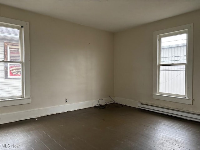 empty room with a baseboard radiator, dark wood-type flooring, and a healthy amount of sunlight