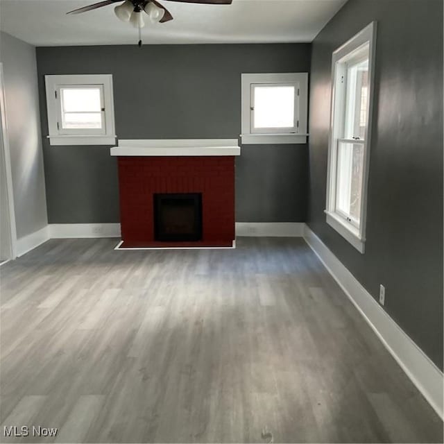 unfurnished living room with a brick fireplace, hardwood / wood-style floors, and ceiling fan