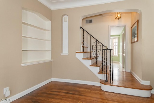 stairway with hardwood / wood-style flooring, crown molding, and built in features