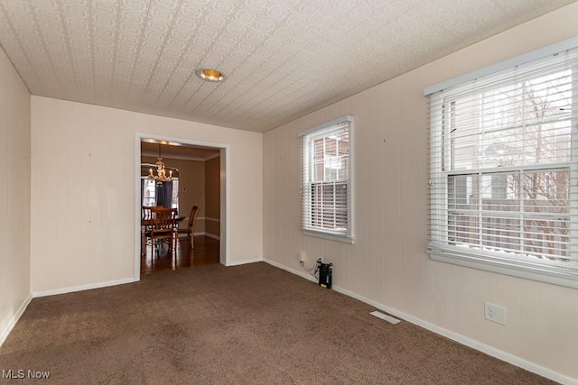 unfurnished room with a chandelier, a wealth of natural light, and dark carpet