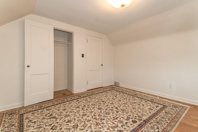 unfurnished bedroom featuring vaulted ceiling, hardwood / wood-style floors, and a closet