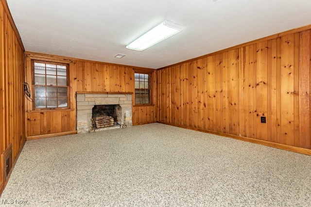 unfurnished living room featuring crown molding, wooden walls, a stone fireplace, and carpet