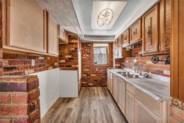 kitchen featuring brick wall, sink, a textured ceiling, and light wood-type flooring