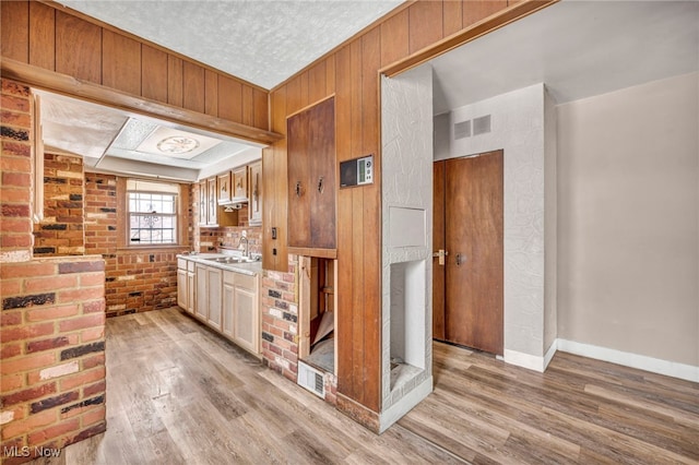 kitchen featuring brick wall, sink, a textured ceiling, and light wood-type flooring