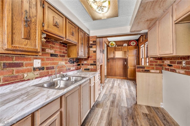 kitchen featuring brick wall, sink, a textured ceiling, and light hardwood / wood-style flooring