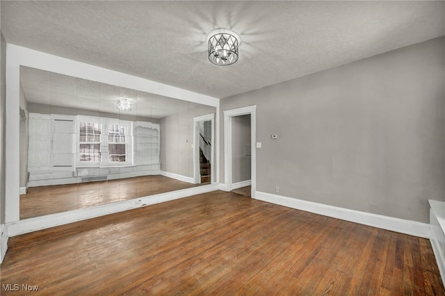 unfurnished living room with wood-type flooring, an inviting chandelier, and a textured ceiling