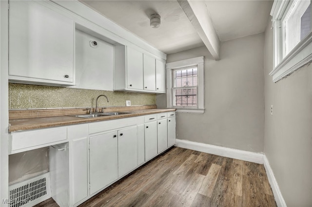 kitchen featuring sink, white cabinets, backsplash, hardwood / wood-style flooring, and beam ceiling