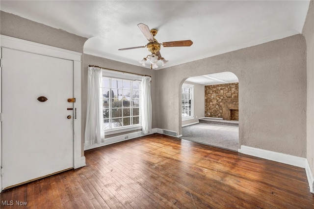 entryway with a stone fireplace, wood-type flooring, and ceiling fan