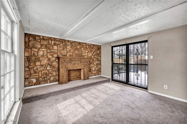 unfurnished living room featuring carpet flooring, a stone fireplace, beam ceiling, and a textured ceiling