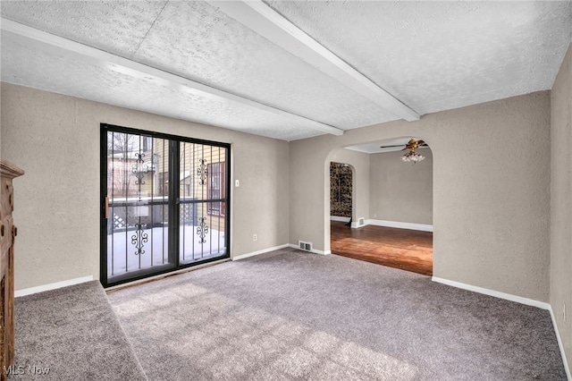 empty room featuring beamed ceiling, ceiling fan, carpet floors, and a textured ceiling