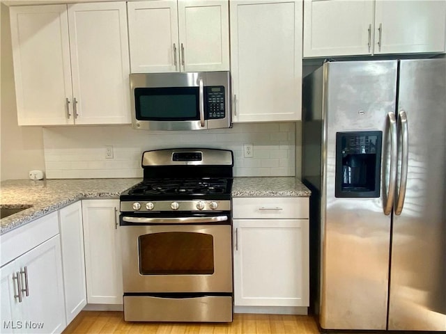 kitchen featuring white cabinetry, light stone counters, appliances with stainless steel finishes, light hardwood / wood-style floors, and backsplash