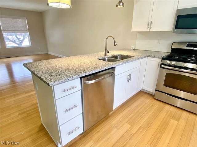 kitchen with sink, appliances with stainless steel finishes, kitchen peninsula, light stone countertops, and white cabinets