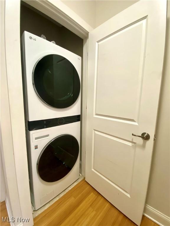 clothes washing area with light hardwood / wood-style floors and stacked washer / dryer