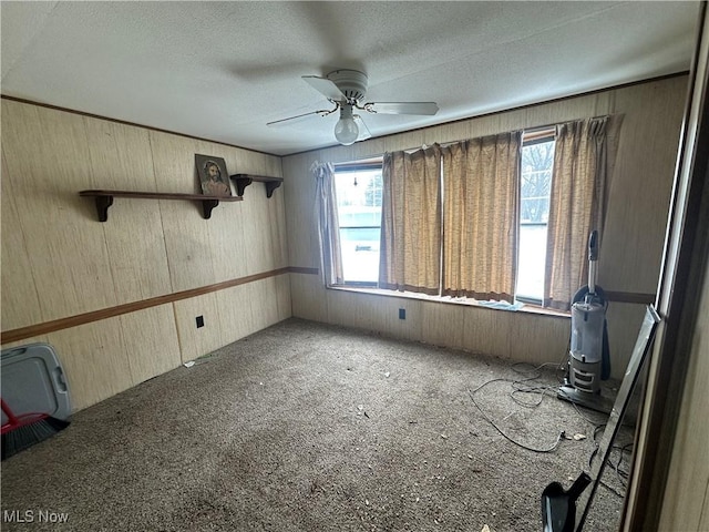 empty room featuring a textured ceiling, wood walls, ceiling fan, and carpet flooring