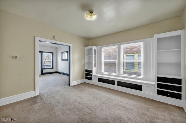 unfurnished living room featuring a healthy amount of sunlight, light carpet, and built in features