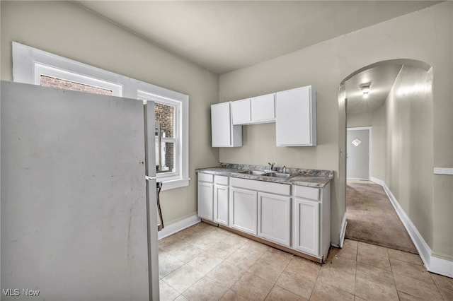 kitchen with white cabinets, sink, light tile patterned floors, and stainless steel fridge