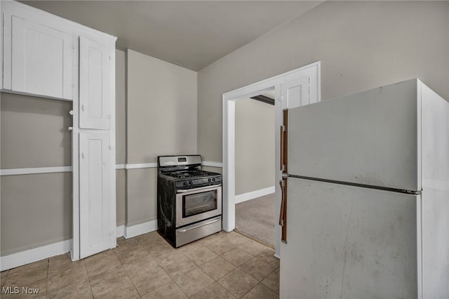 kitchen with white refrigerator, white cabinetry, stainless steel gas range, and light tile patterned floors