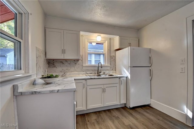 kitchen featuring sink, light hardwood / wood-style flooring, white refrigerator, white cabinets, and backsplash