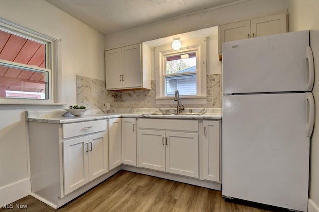 kitchen with white refrigerator, light wood-type flooring, sink, and white cabinets