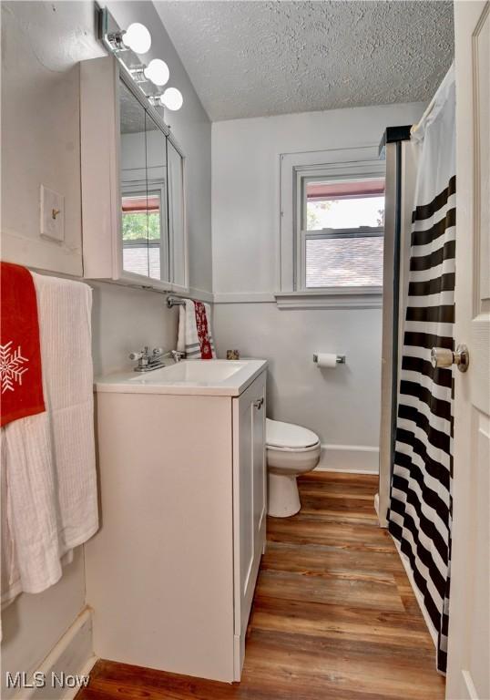 bathroom featuring toilet, hardwood / wood-style floors, a textured ceiling, and a wealth of natural light