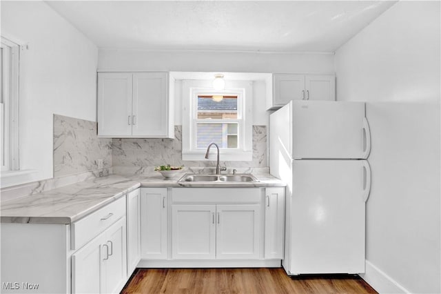 kitchen with tasteful backsplash, white cabinetry, sink, white fridge, and light hardwood / wood-style flooring