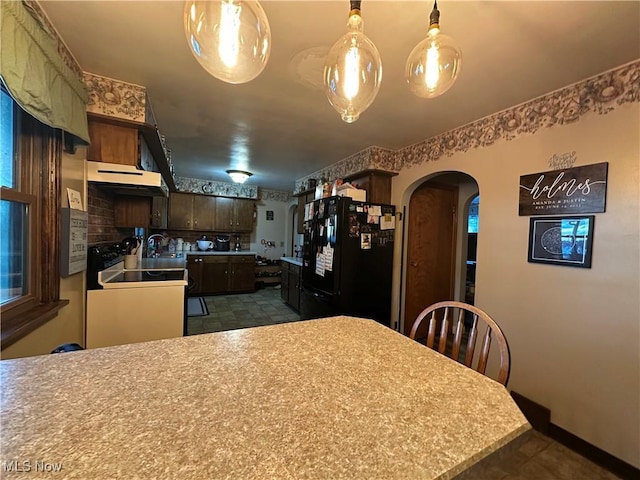 kitchen featuring sink, range, dark brown cabinets, black fridge, and kitchen peninsula