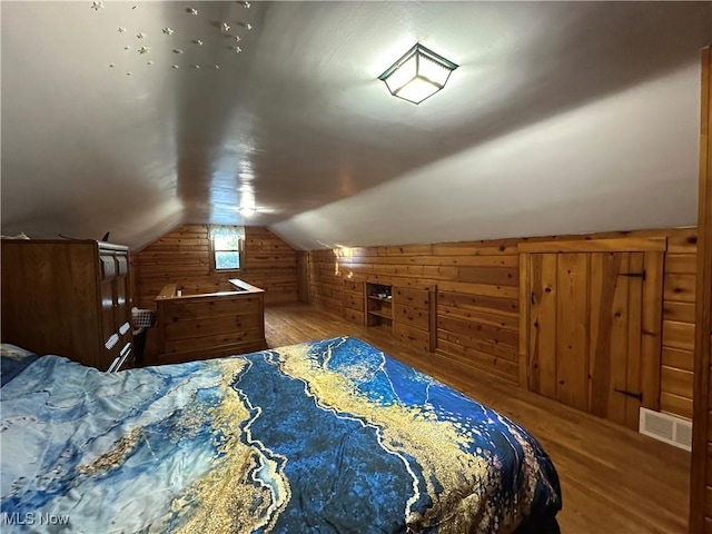 bedroom featuring lofted ceiling, wooden walls, and wood-type flooring