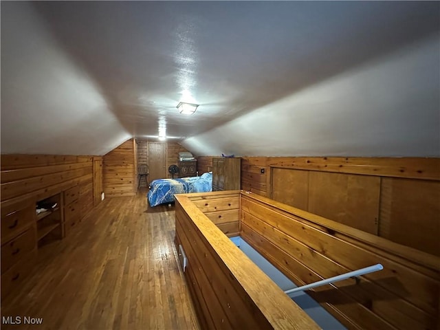 unfurnished bedroom with hardwood / wood-style flooring, vaulted ceiling, and wood walls