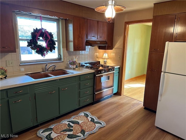 kitchen with sink, gas range, white fridge, light hardwood / wood-style floors, and decorative backsplash