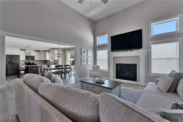 living room featuring ceiling fan, a tiled fireplace, a high ceiling, and light wood-type flooring