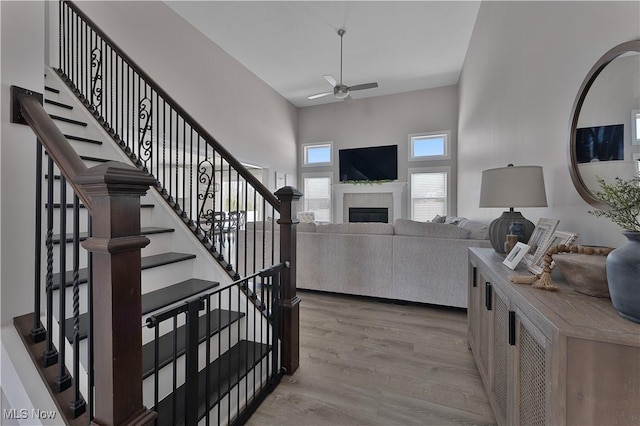 entrance foyer with a tiled fireplace, a high ceiling, ceiling fan, and light hardwood / wood-style flooring