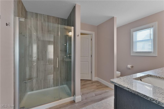 bathroom featuring wood-type flooring, vanity, an enclosed shower, toilet, and a textured ceiling