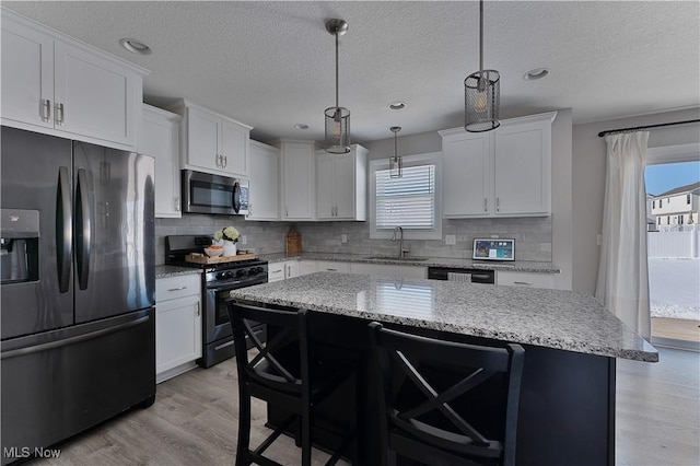 kitchen with sink, black appliances, white cabinets, a kitchen island, and decorative light fixtures