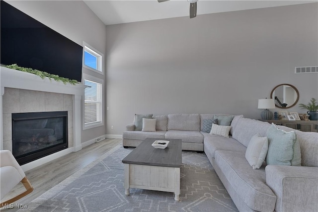 living room with hardwood / wood-style flooring, a tile fireplace, ceiling fan, and a high ceiling