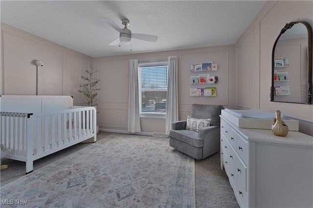 bedroom with a nursery area, light colored carpet, ceiling fan, and a textured ceiling