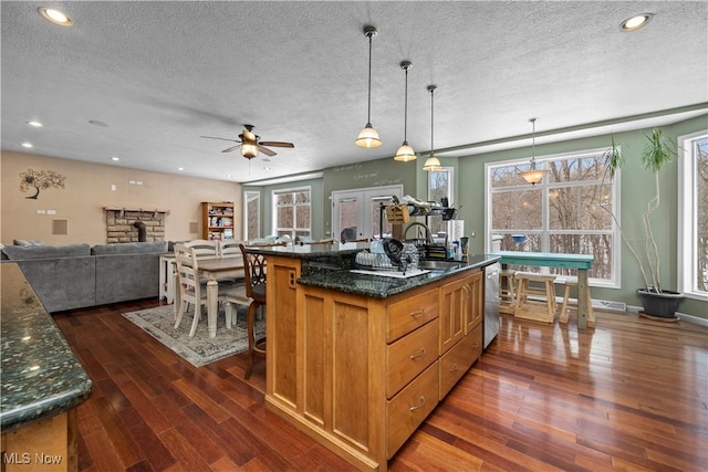 kitchen featuring decorative light fixtures, an island with sink, sink, dark stone counters, and stainless steel dishwasher