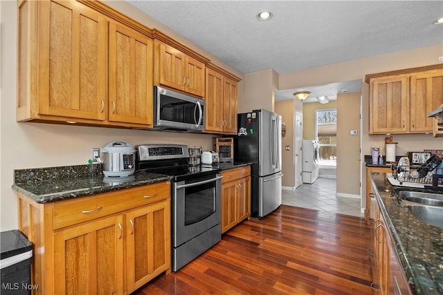 kitchen featuring appliances with stainless steel finishes, sink, dark hardwood / wood-style flooring, and dark stone counters