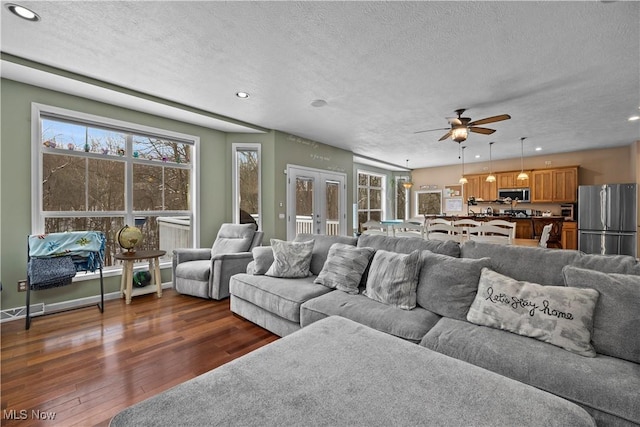 living room with ceiling fan, a textured ceiling, dark hardwood / wood-style flooring, and french doors